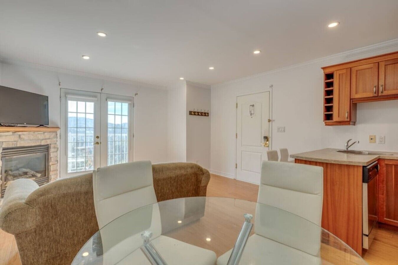 A living room with a glass table and two chairs, a fireplace, and a kitchen with wooden cabinets.