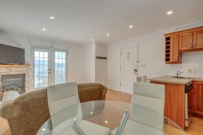 Un salon moderne avec une table en verre, deux canapés, une cheminée et un coin cuisine doté de meubles en bois.