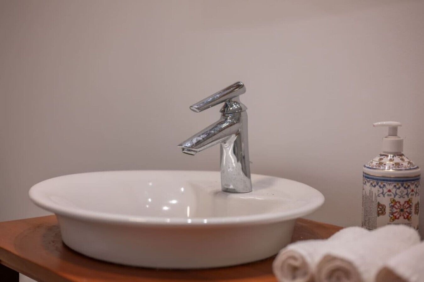 A bathroom sink with a modern faucet, a decorative soap dispenser, and a rolled towel on a wooden surface.