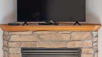 A flat-screen TV mounted on a wooden mantel above a stone fireplace with a glass door.