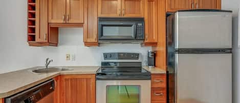 Una cocina con armarios de madera, microondas, refrigerador de acero inoxidable, lavavajillas y estufa.