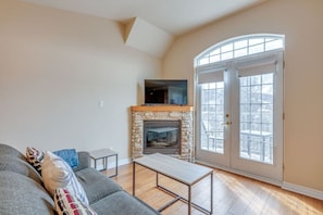 A living room with a stone fireplace, a flat-screen TV, a gray sofa, and a wooden coffee table.