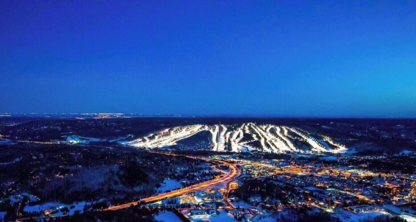 Vista aérea nocturna de una ciudad con una montaña destacada al fondo.