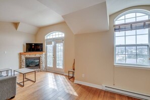 A spacious living room with hardwood flooring, a stone fireplace, a television, and large windows. - Condo Alpina - 3302 | Détente à St-Sauveur (Piedmont)