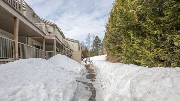 Un sendero cubierto de nieve que conduce a un edificio con un balcón y una barrera de nieve a un lado.
