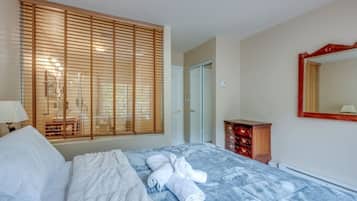 A hotel room with a bed, a wooden dresser, a mirror, and a window with blinds.