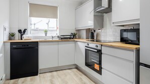 Een moderne keuken met witte kasten, een houten aanrecht, een vaatwasser, een oven en een magnetron.