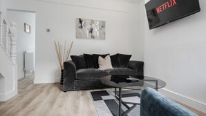Een moderne woonkamer met een grijze bank, een glazen salontafel en een tv met daarop 'NETFLIX'.