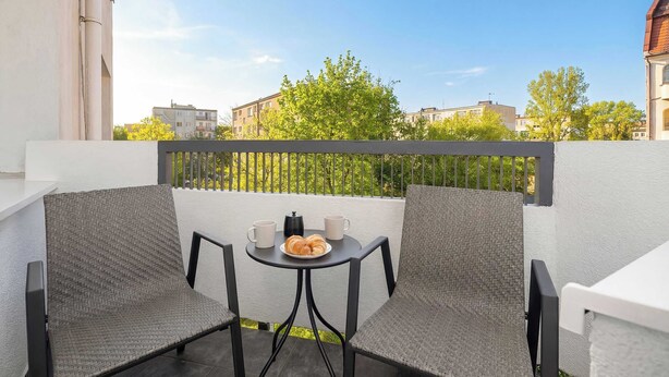 Un balcon avec deux chaises grises, une petite table ronde et une assiette contenant des croissants et deux tasses blanches.