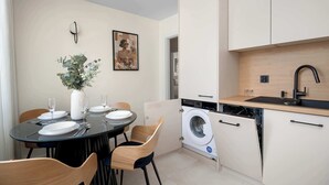 Une cuisine compacte équipée d’un lave-linge, d’une table à manger avec assiettes et verres, et d’un tableau accroché au mur.