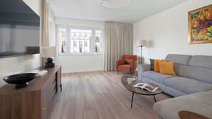 Un salon moderne comprenant un canapé, un fauteuil, une table basse et un téléviseur à écran plat.
