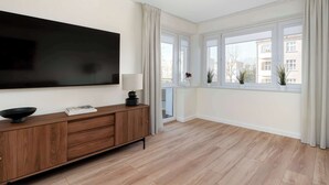 Un salon moderne doté d’un téléviseur à écran plat, d’un meuble en bois et de grandes fenêtres avec des rideaux.