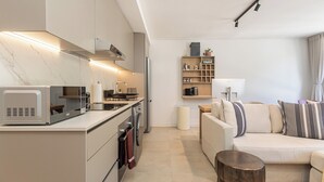 Una cocina moderna con microondas, estufa y horno, un espacio de sala con sofá y mesa de centro, y un estante pequeño con adornos.