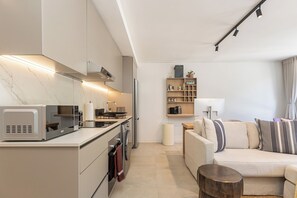 Eine moderne Küche mit Mikrowelle, Herd und Backofen, ein Wohnbereich mit Sofa und Couchtisch sowie ein kleines Regal mit Dekoration.
