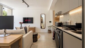 Una cocina moderna con horno empotrado, un lavamanos y una zona de comedor con un televisor mostrando 'NETFLIX'.