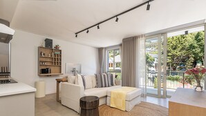 Una sala de estar moderna con un sofá, una mesa de centro, una mesita auxiliar, una estantería y un amplio ventanal corredero que da a un espacio exterior.