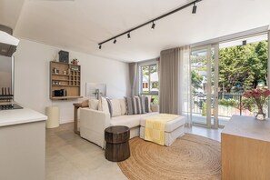 Ein modernes Wohnzimmer mit einer Couch, einem Couchtisch, einem Beistelltisch, einem Bücherregal und einer großen Glasschiebetür, die zu einem Außenbereich führt.