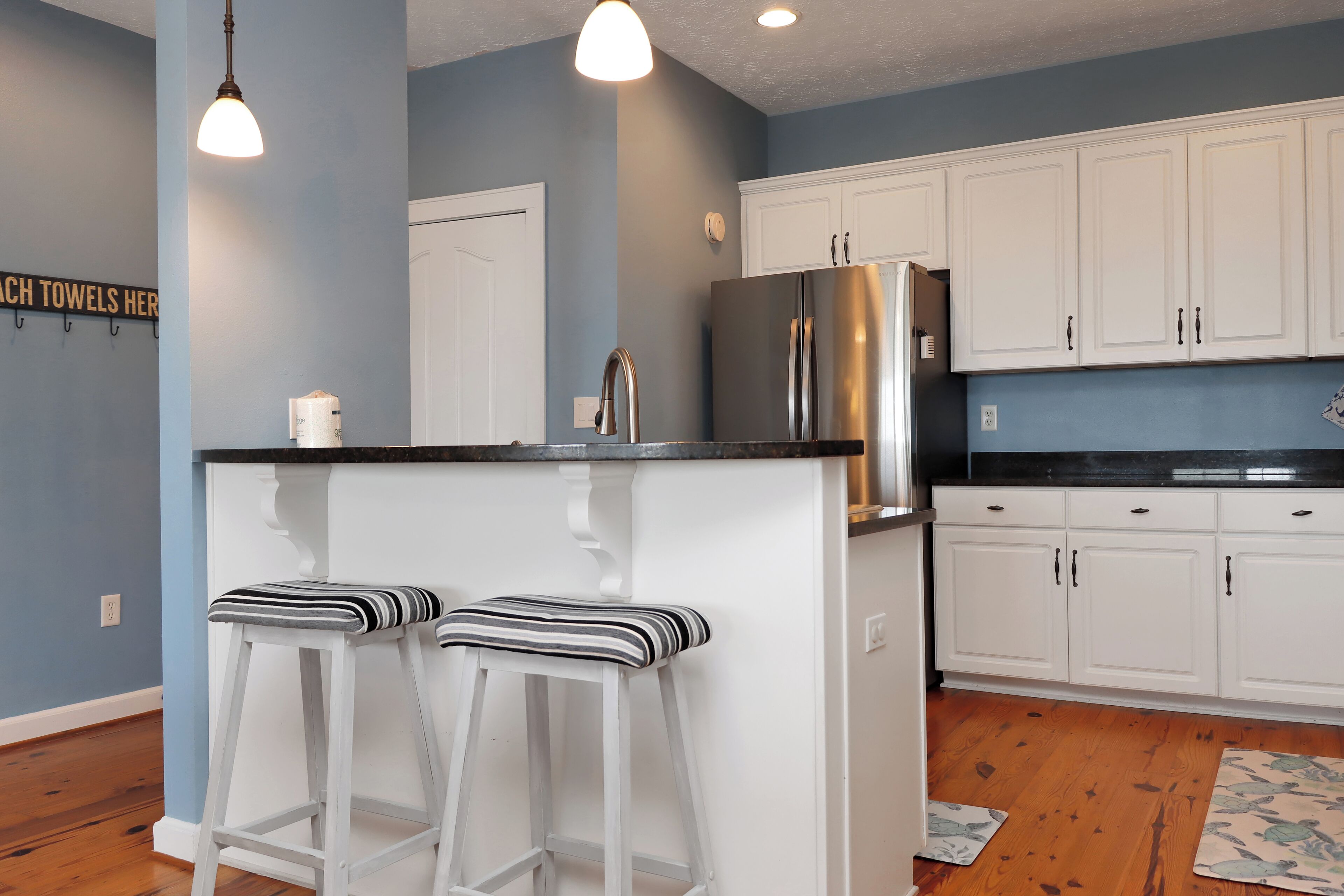 A kitchen with white cabinets, a stainless steel refrigerator, and two bar stools with striped cushions.