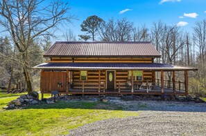 A log cabin with a porch, a front door, and a small front yard. - Caney Creek Retreat 1 Bedroom Cabin (Cosby)