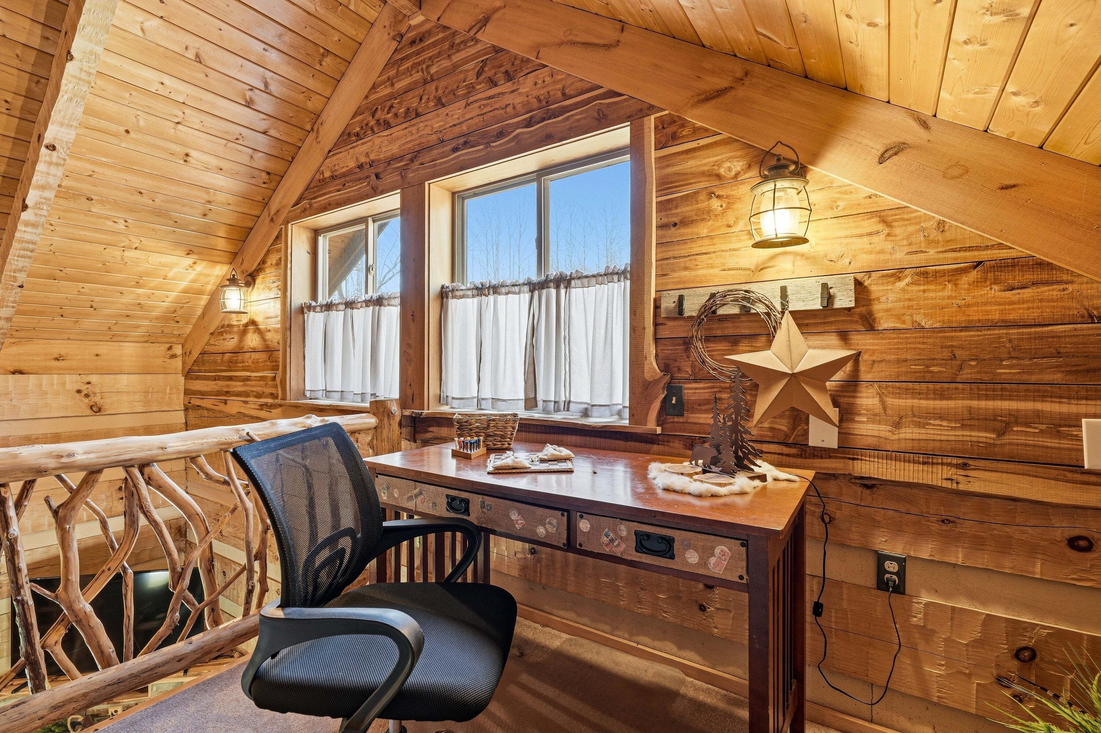 Interno di una baita in legno con una scrivania, una sedia, finestre e una decorazione a forma di stella.