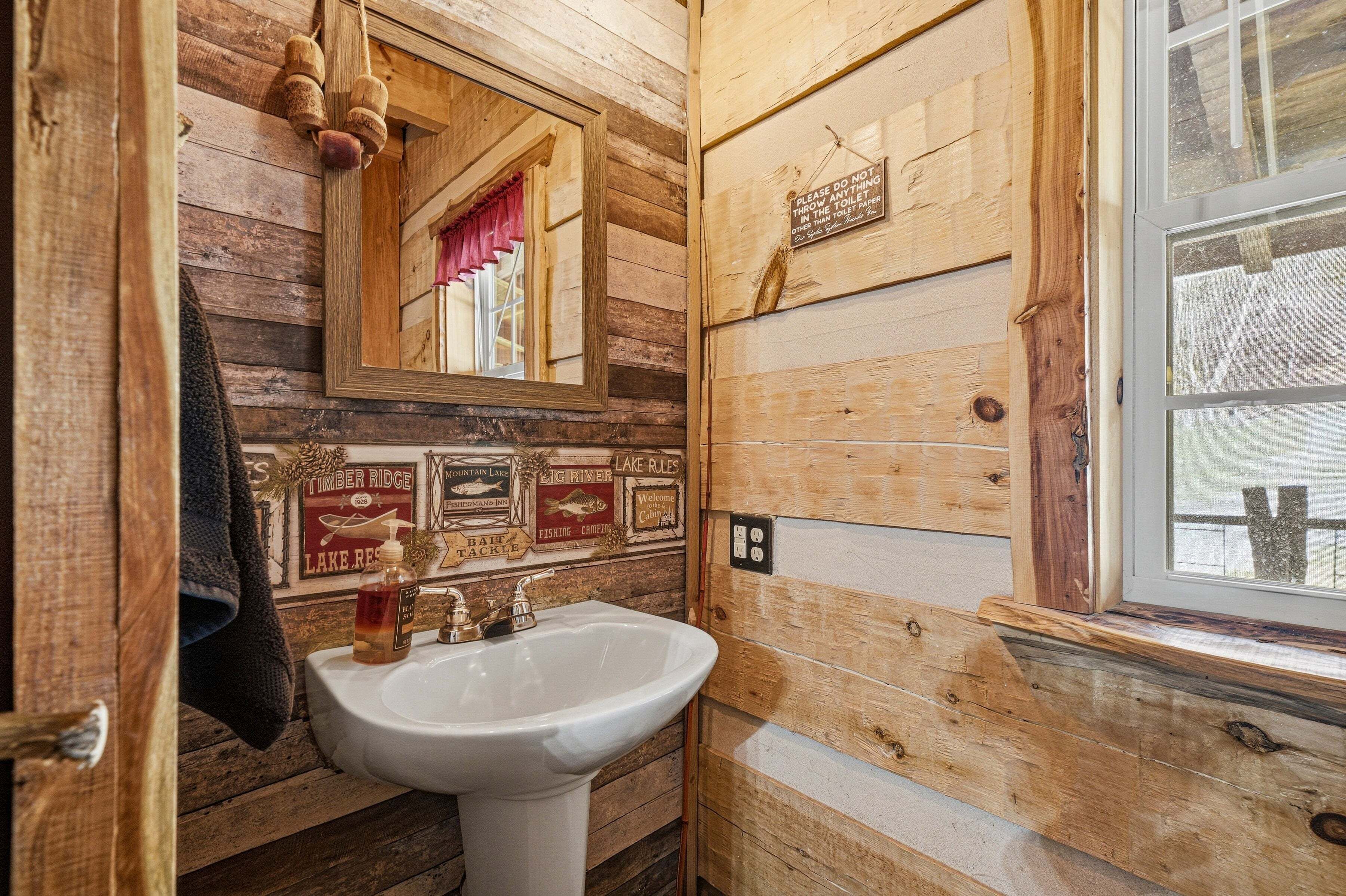 A rustic wooden bathroom with a sink, mirror, and a window.
