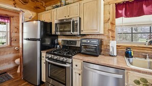 A compact kitchen with wooden cabinets, a stainless steel refrigerator, a microwave, a stove, and a dishwasher. - Caney Creek Retreat 1 Bedroom Cabin (Cosby)