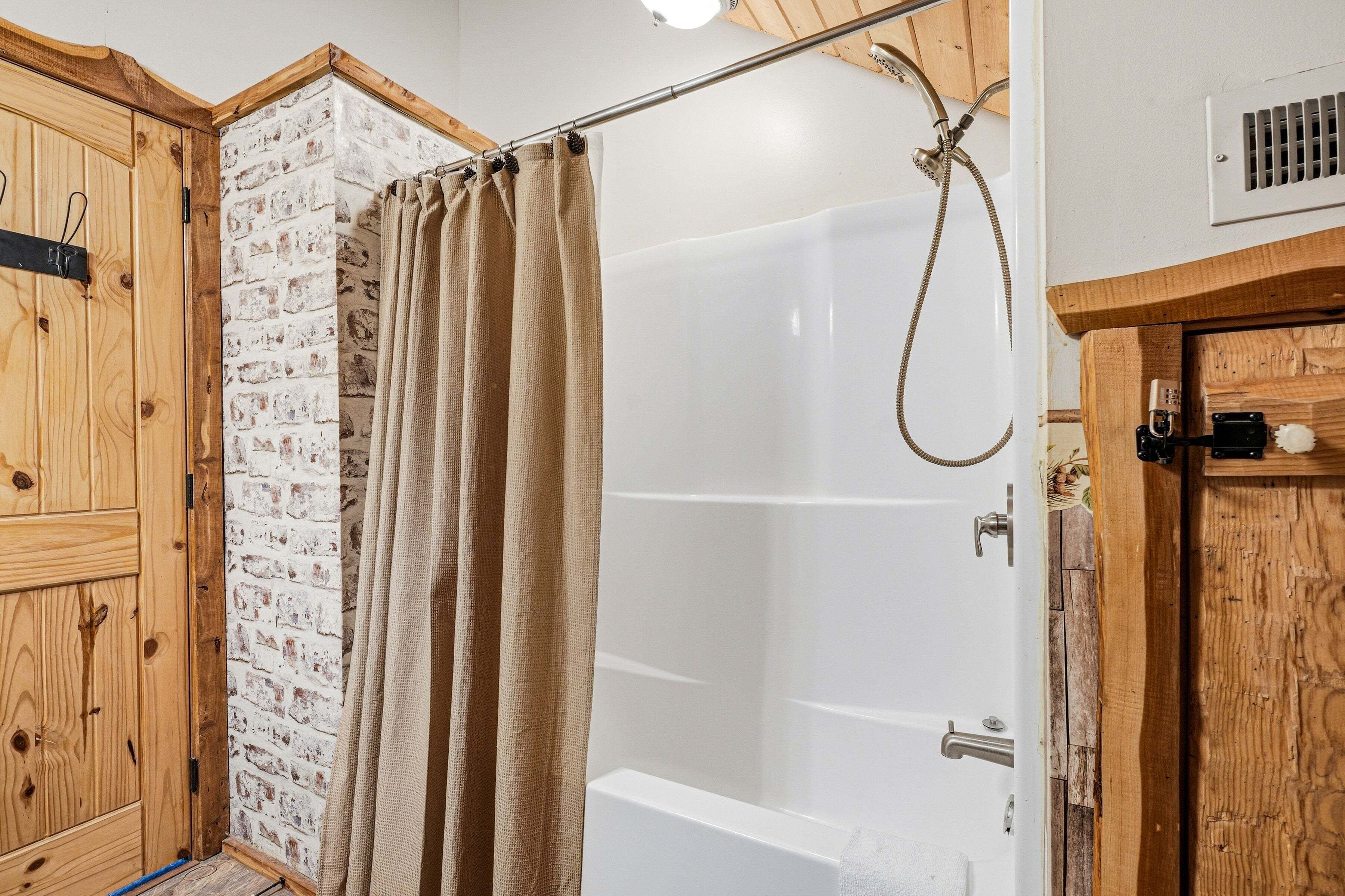 A shower area with a curtain, a bathtub, and wooden cabinetry.