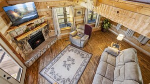 A cozy cabin interior with a stone fireplace, a television, a sofa, and a dining area. - Caney Creek Retreat 1 Bedroom Cabin (Cosby)
