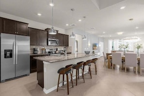 A modern kitchen with a central island, bar stools, stainless steel appliances, pendant lighting, and a dining area with chairs. - 7 Bedroomss/ Windsor Cay Home (Clermont)