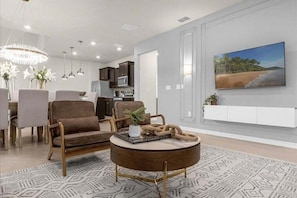 A modern living room with a round coffee table, a dining area with chairs, a kitchen in the background, and a large painting on the wall. - 7 Bedroomss/ Windsor Cay Home (Clermont)