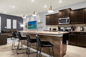 A modern kitchen with dark wood cabinets, a central island with bar stools, a microwave, and a coffee maker. - 10 Bedroomss/ Windsor Island Home (Davenport)