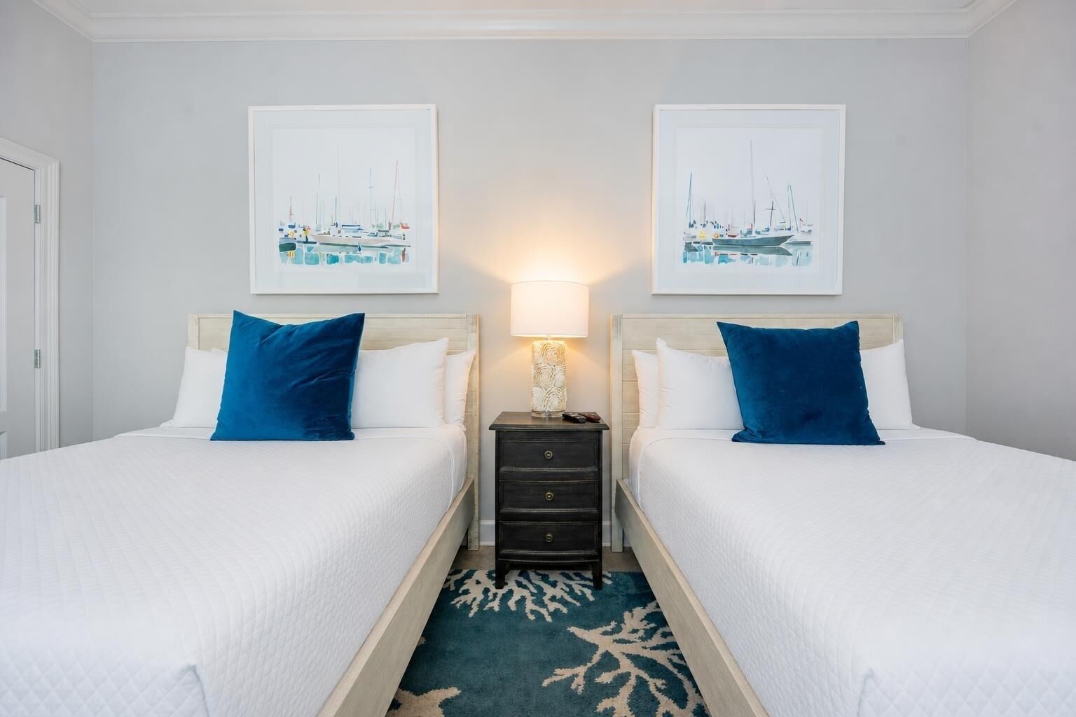 Une chambre d’hôtel avec deux lits, une table de chevet, une lampe et deux tableaux encadrés au mur.