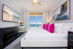 Ein Hotelzimmer mit einem großen Bett, einem Deckenventilator, Meerblick, einem Schreibtisch mit Schubladen und einem Sessel.