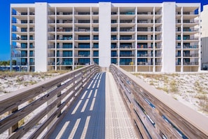 Un hôtel à plusieurs étages doté de balcons, une promenade en bois menant à l’hôtel et, en arrière-plan, une plage de sable.