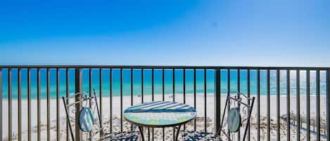 A balcony with a view of the beach, two chairs, and a small table.
