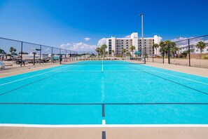 A swimming pool with a clear blue surface, surrounded by a fence, with a hotel building in the background. - Wind Drift 604s 2 Bedroom Condo (Orange Beach)