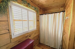 L’intérieur d’un chalet en bois, avec une fenêtre dotée de volets, un rideau et un petit banc rouge.