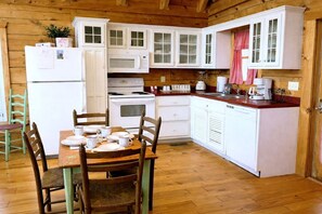 A wooden interior with a kitchen area, including white cabinets, a refrigerator, a stove, and a dining table with chairs. - Adorable Shut'er Inn 1 Bedroom Cabin (Pigeon Forge)