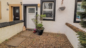 A building with a white exterior, a black door, and a window with a metal grill. - 25 Low Seaton (Workington)