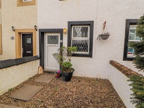 A building with a white exterior, a black door, and a window with a metal grill. - 25 Low Seaton (Workington)