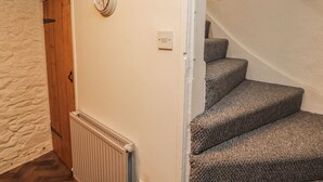 A staircase with carpeted steps, a wooden door, a wall clock, and a radiator. - 25 Low Seaton (Workington)