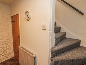 A staircase with carpeted steps, a wooden door, a wall clock, and a radiator. - 25 Low Seaton (Workington)