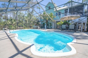 Una piscina con cerramiento de vidrio, rodeada de mobiliario exterior y una casa al fondo.