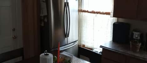 A kitchen with wooden cabinets, a refrigerator, a microwave, and a window with curtains.