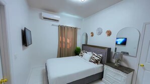 Une chambre à coucher comprenant un lit, une table de chevet, un téléviseur, un miroir et un appareil de climatisation.