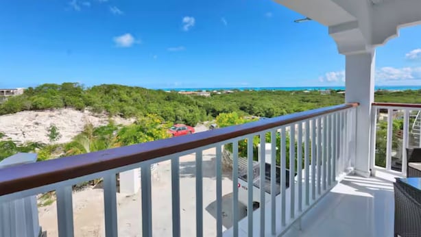A balcony with a white railing overlooking a beach and ocean.