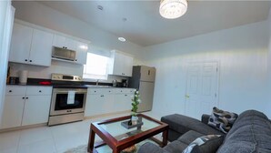 A modern kitchen with white cabinets, a built-in oven, and a microwave. There is a gray sofa with patterned cushions and a glass coffee table.