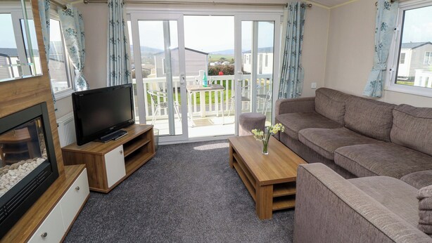 A living room with a sofa, a TV, a fireplace, and a balcony with a view. - 63 Crosswinds (Bembridge)