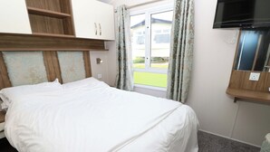 A hotel room with a bed, a television, a window with curtains, and a view of a house outside. - 63 Crosswinds (Bembridge)