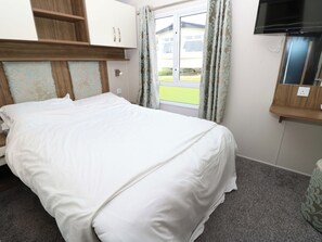 A hotel room with a bed, a television, a window with curtains, and a view of a house outside. - 63 Crosswinds (Bembridge)